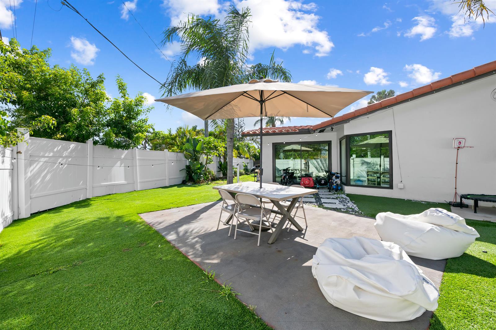 A backyard patio features a dining table with an umbrella, beanbag chairs, and artificial turf — 2601 NE 8th Court, Pompano Beach FL 33062, POMPANO BEACH, FL