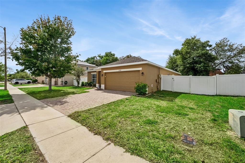 A tan house with a two-car garage and a white vinyl fence on a corner lot — 240 WHISPERING PINES WAY, DAVENPORT, FL