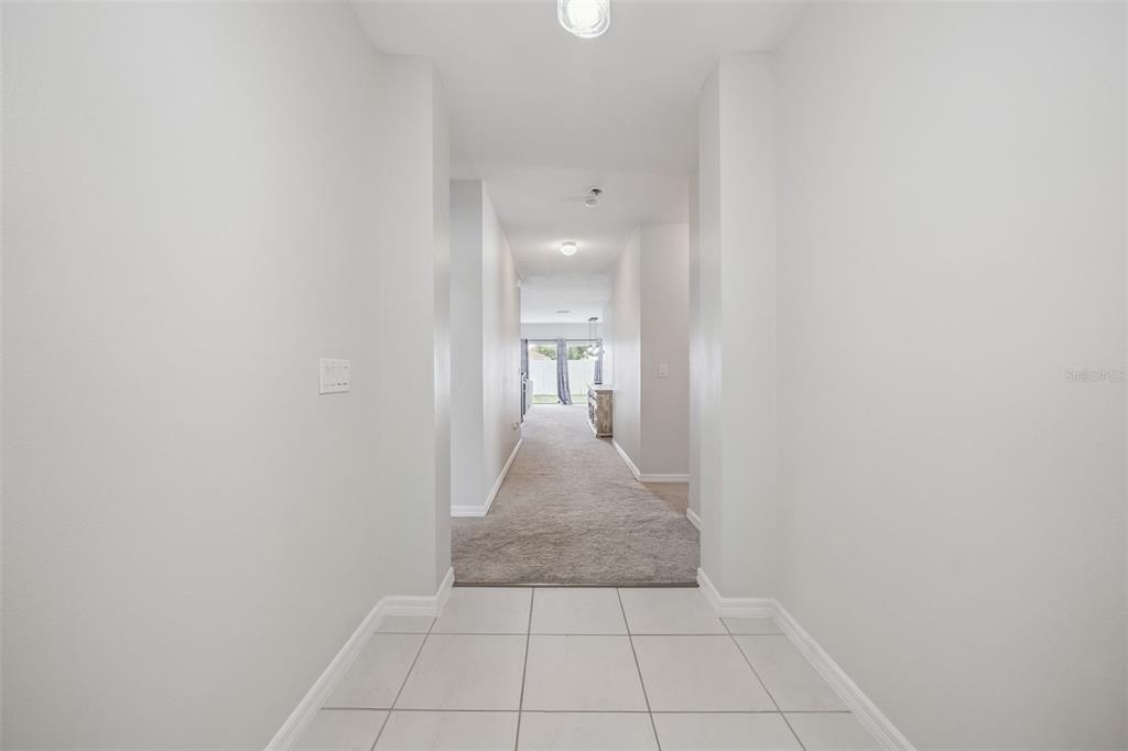 A hallway with white tile flooring transitions into a carpeted living area with natural light — 240 WHISPERING PINES WAY, DAVENPORT, FL