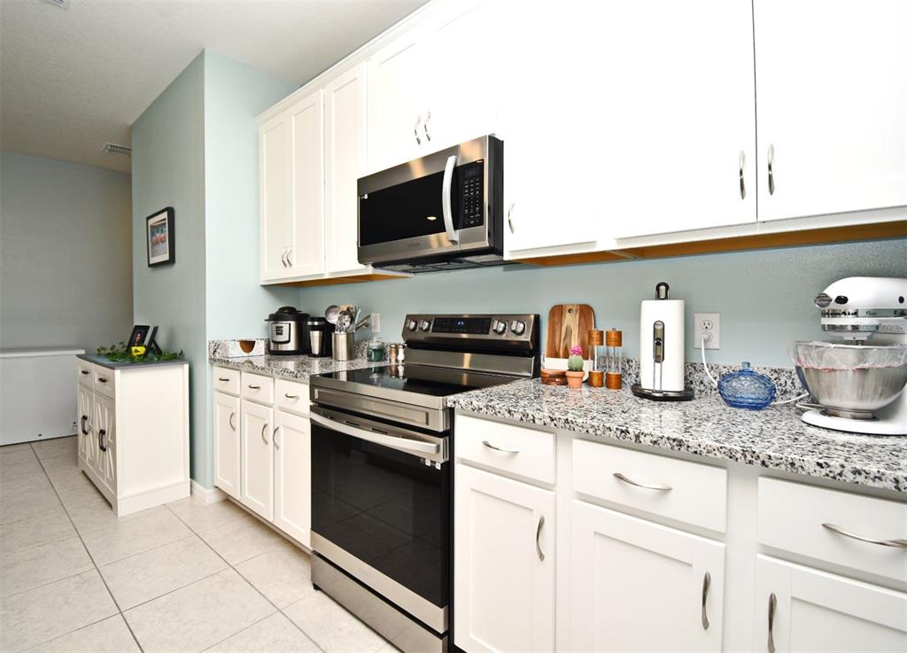 A kitchen features white cabinetry, granite countertops, and stainless steel appliances — 33291 REMBRANDT LANE, SORRENTO, FL