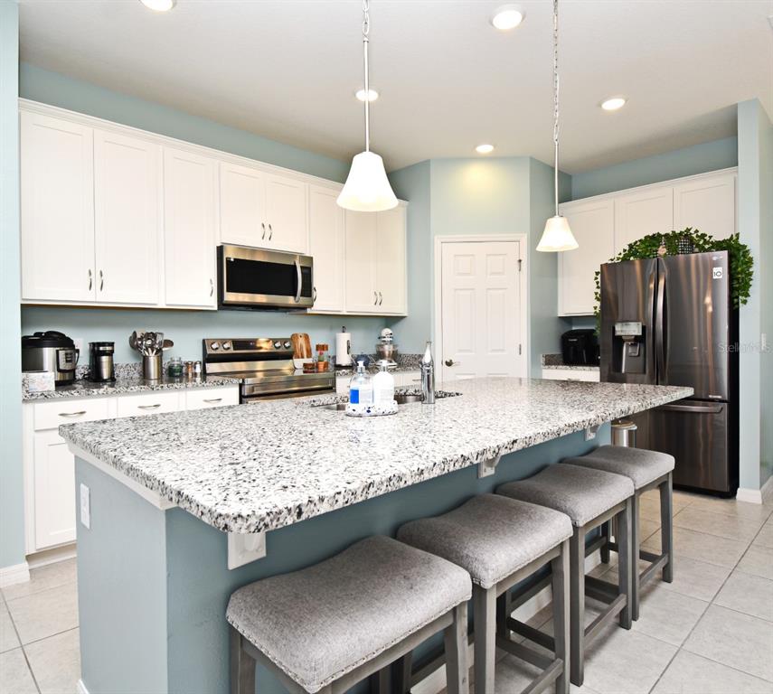 A kitchen features white cabinets, granite countertops, a central island with bar seating, and stainless appliances — 33291 REMBRANDT LANE, SORRENTO, FL