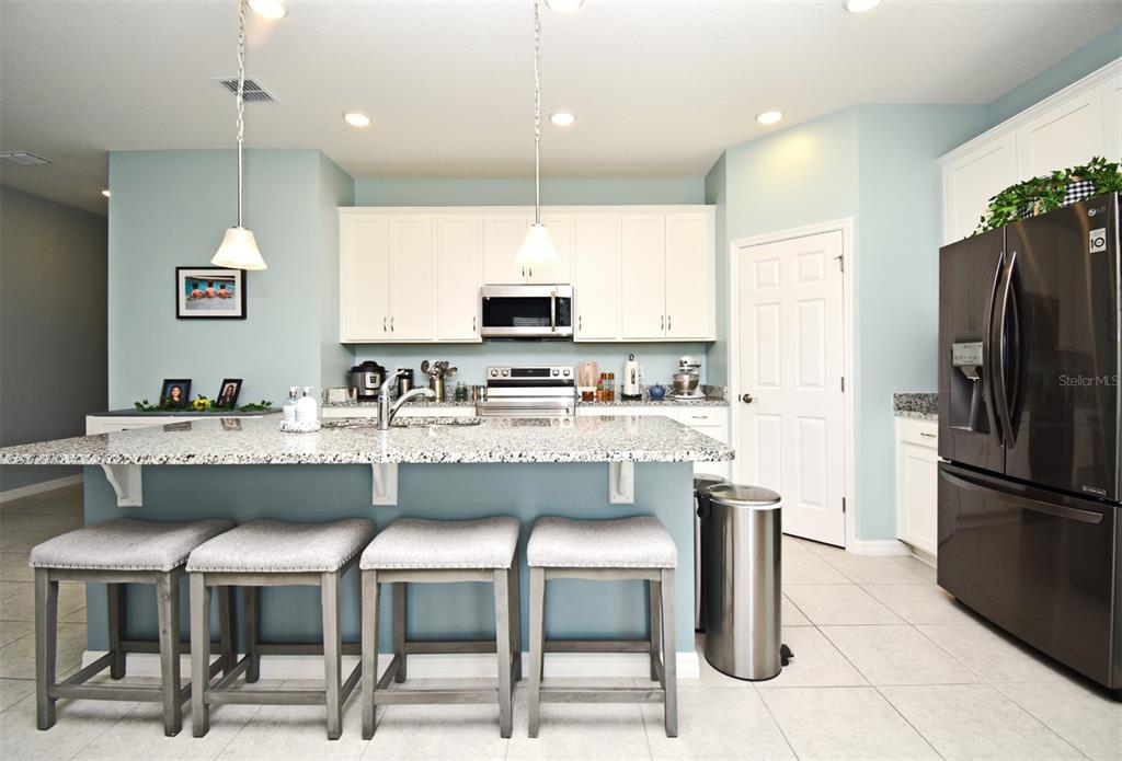 A kitchen features a granite-topped island with four stools, white cabinetry, and stainless steel appliances — 33291 REMBRANDT LANE, SORRENTO, FL