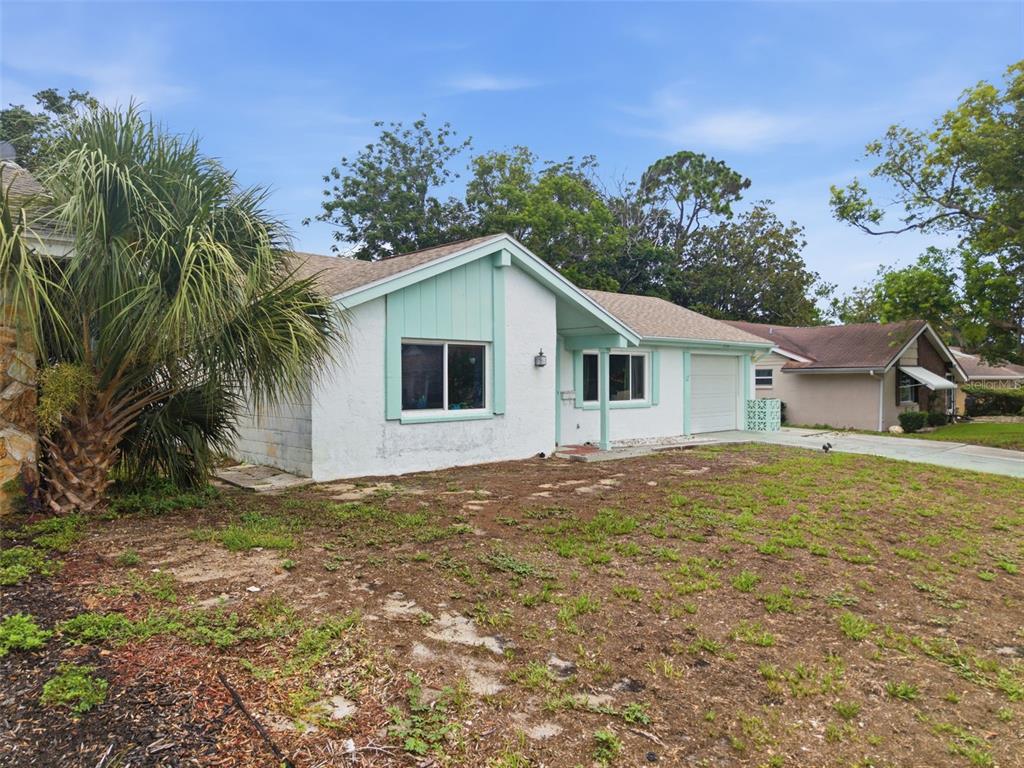 A single-story house with white stucco walls, light green trim, and a patchy grass yard — 12305 PARTRIDGE HILL ROW, HUDSON, FL