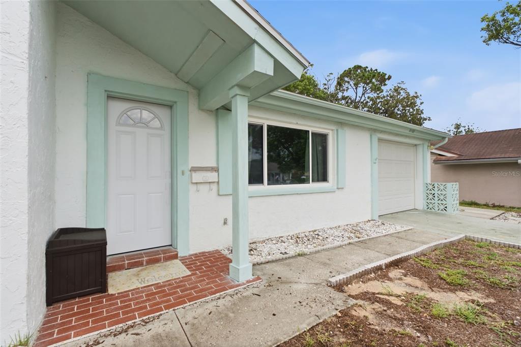 A white house exterior features a brick entryway, light green trim, and a single-car garage — 12305 PARTRIDGE HILL ROW, HUDSON, FL