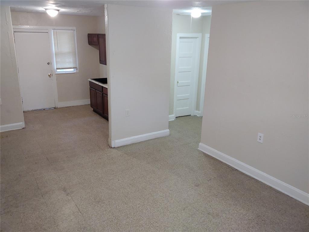 An interior view shows a carpeted room with a doorway leading to a small kitchen area — 1911 W 26TH STREET, JACKSONVILLE, FL