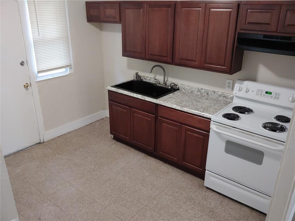 A kitchen features dark wood cabinets, a black sink, white appliances, and light-colored countertops — 1911 W 26TH STREET, JACKSONVILLE, FL