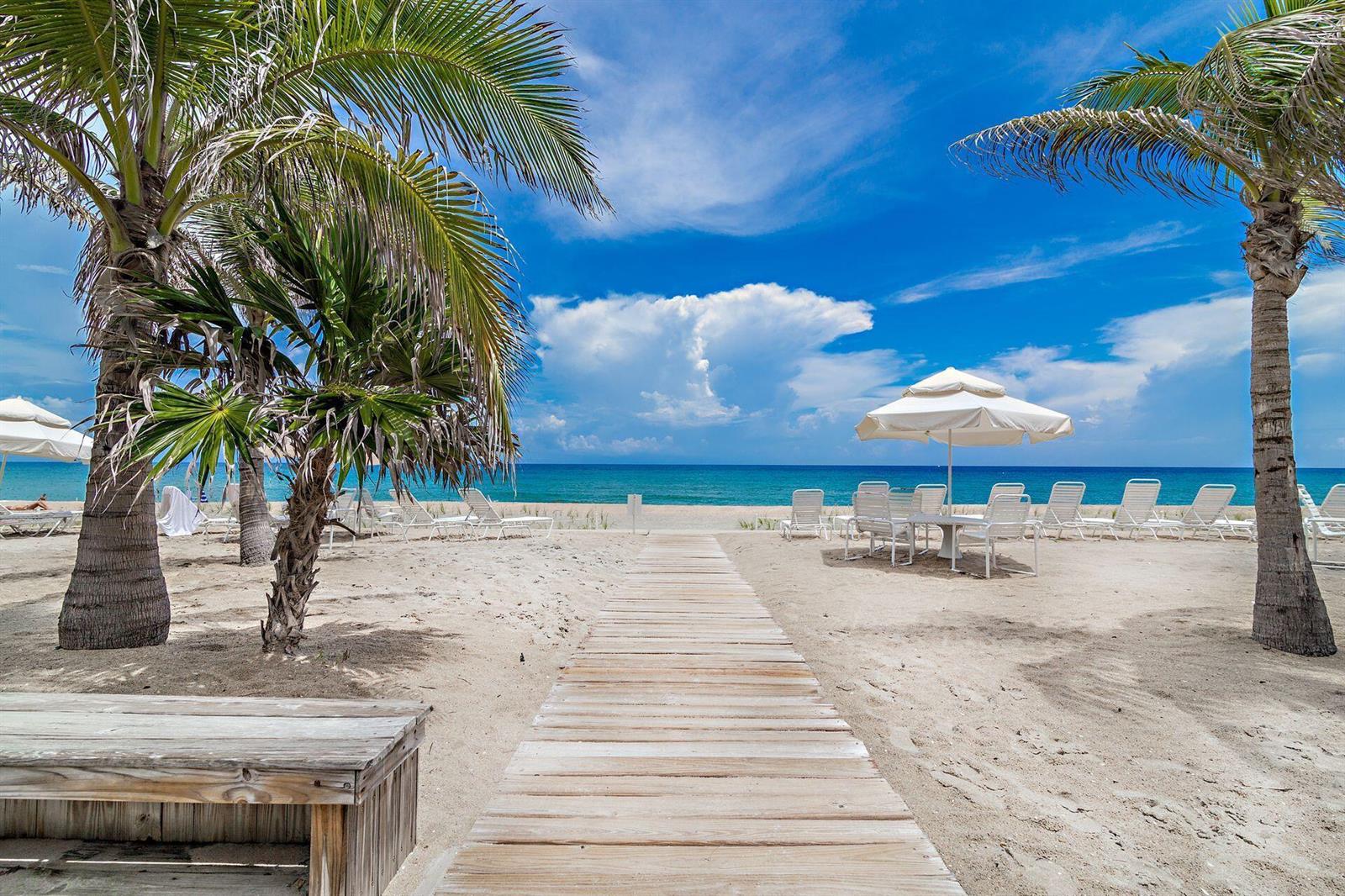 A wooden boardwalk leads through a sandy beach with palm trees and white patio umbrellas — 170 N Ocean Boulevard # 409, Palm Beach FL 33480, PALM BEACH, FL