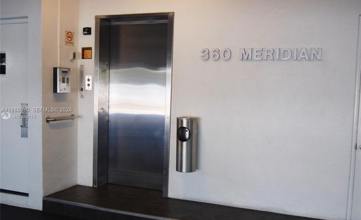 An elevator door is set into a white wall with building signage and a trash receptacle — 360 Meridian Ave # 4C, Miami Beach FL 33139, MIAMI BEACH, FL