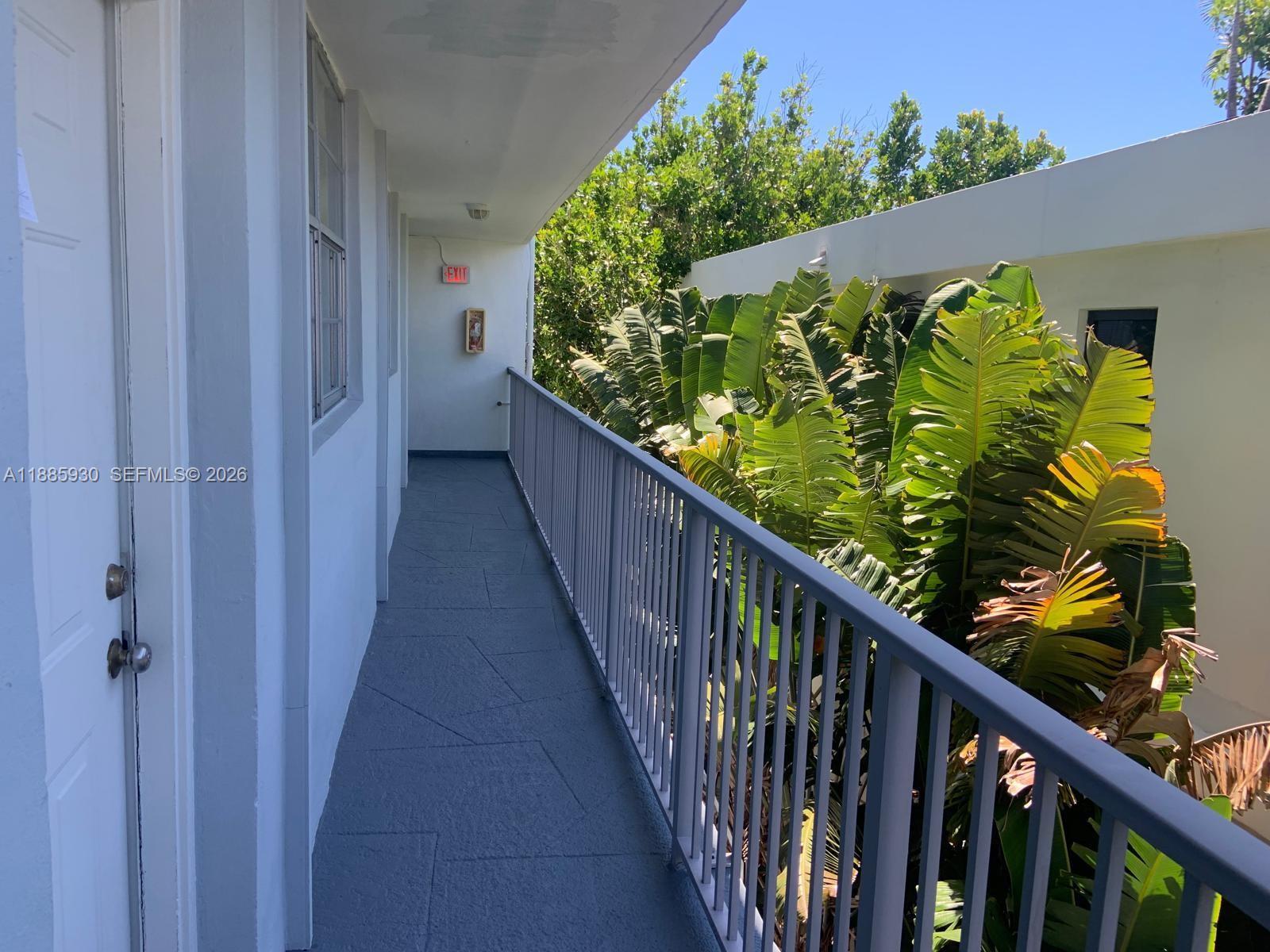 An outdoor walkway with gray flooring and a metal railing overlooks lush green foliage — 360 Meridian Ave # 4C, Miami Beach FL 33139, MIAMI BEACH, FL