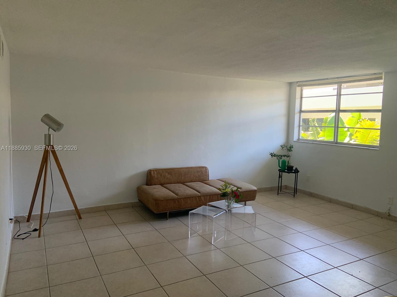 A living room features a tan sofa, acrylic coffee tables, a tripod lamp, and tile flooring — 360 Meridian Ave # 4C, Miami Beach FL 33139, MIAMI BEACH, FL