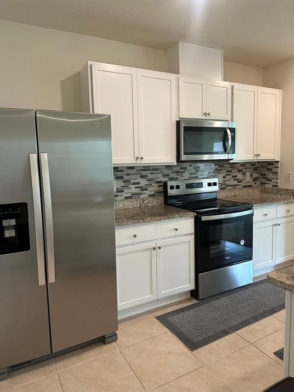 A kitchen features white cabinets, stainless steel appliances, granite countertops, and a tiled backsplash — 2184 DOE RUN DRIVE, DAVENPORT, FL