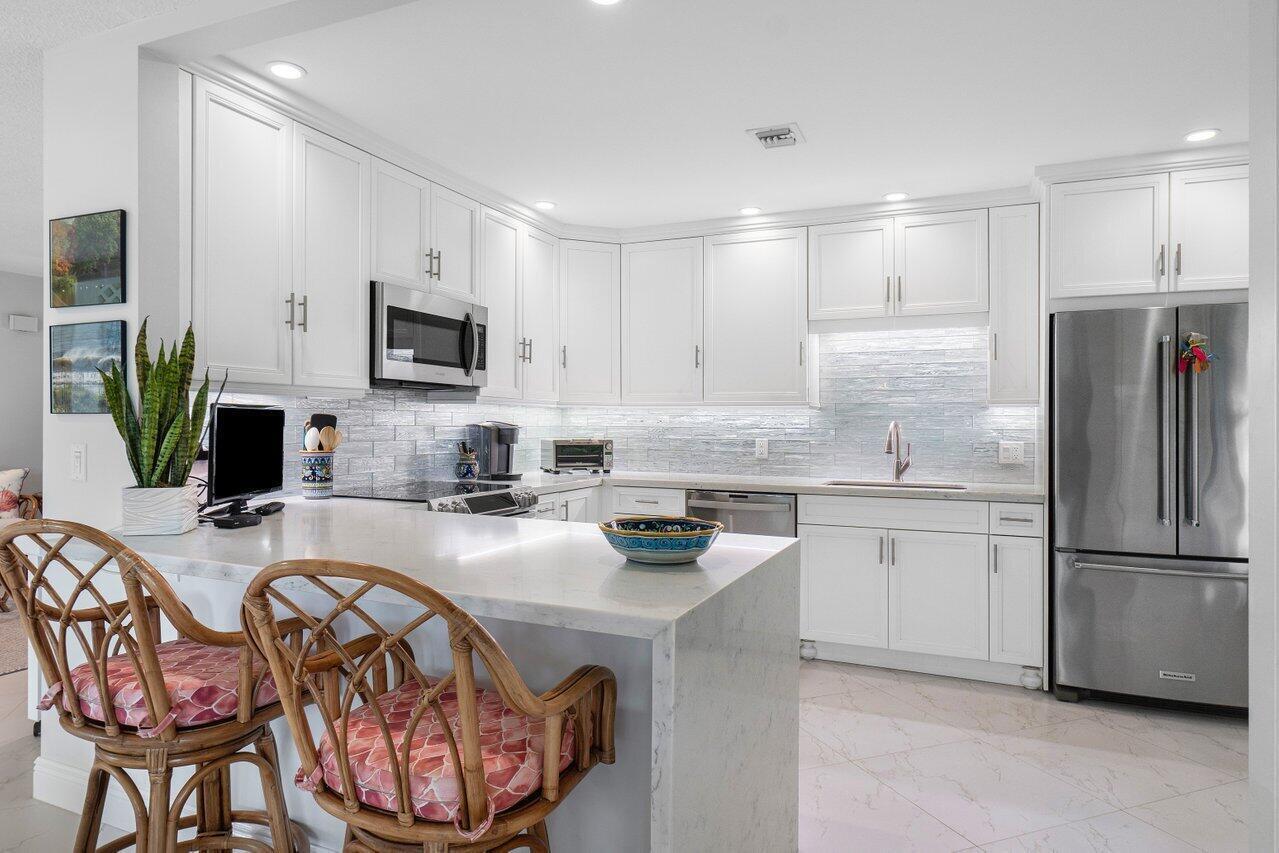 A bright kitchen features white cabinetry, marble countertops, stainless steel appliances, and two rattan stools — 11312 Quail Covey Road, Boynton Beach FL 33436, BOYNTON BEACH, FL