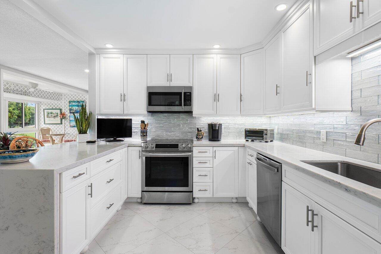 A modern white kitchen features stainless steel appliances, quartz countertops, and a light-colored backsplash — 11312 Quail Covey Road, Boynton Beach FL 33436, BOYNTON BEACH, FL