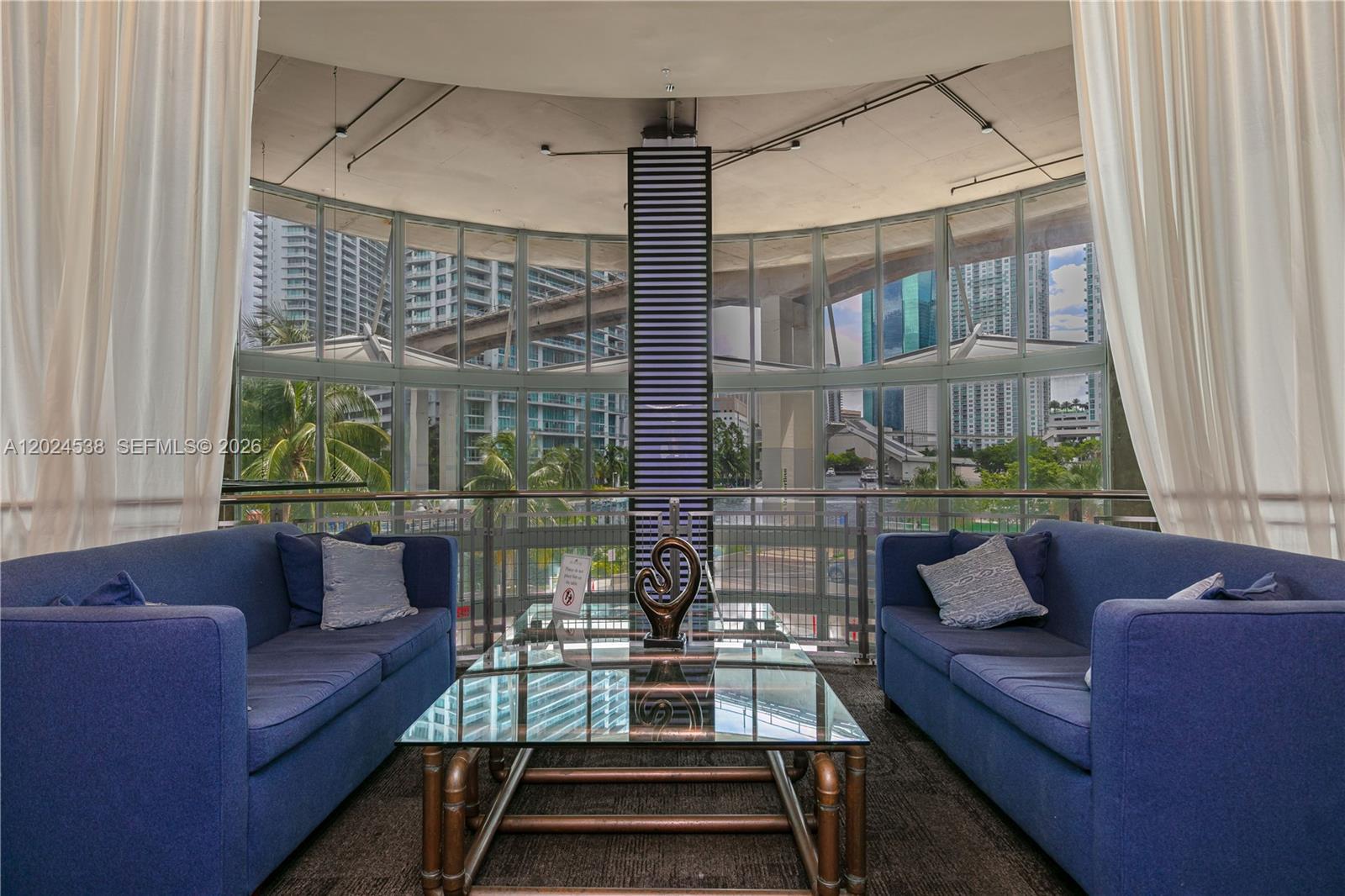A lounge area features two blue sofas facing a glass coffee table before floor-to-ceiling windows — 690 SW 1st Ct, Miami FL 33130, MIAMI, FL