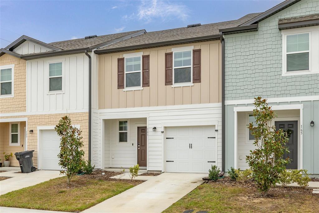 A row of three two-story townhouses with garages, light-colored siding, and small front yards — 161 MANDOVI STREET, DAVENPORT, FL