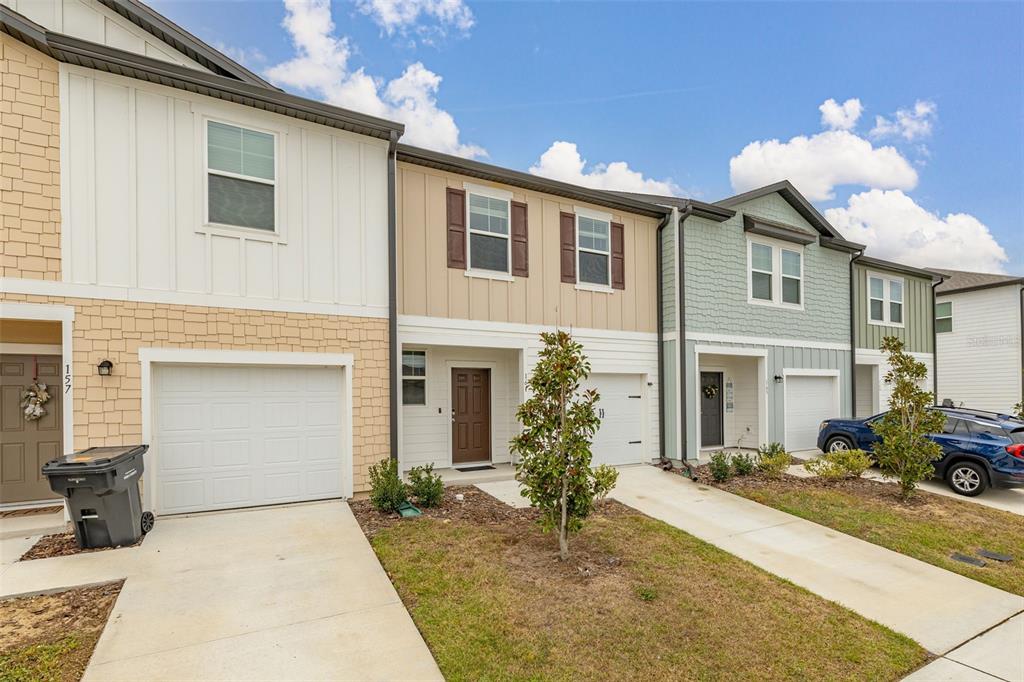 A row of three modern townhomes with attached garages and driveways under a blue sky — 161 MANDOVI STREET, DAVENPORT, FL