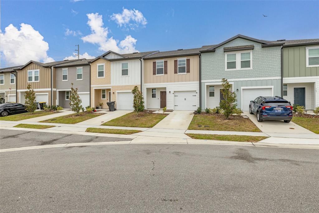 A row of modern two-story townhouses with attached garages and driveways under a blue sky — 161 MANDOVI STREET, DAVENPORT, FL