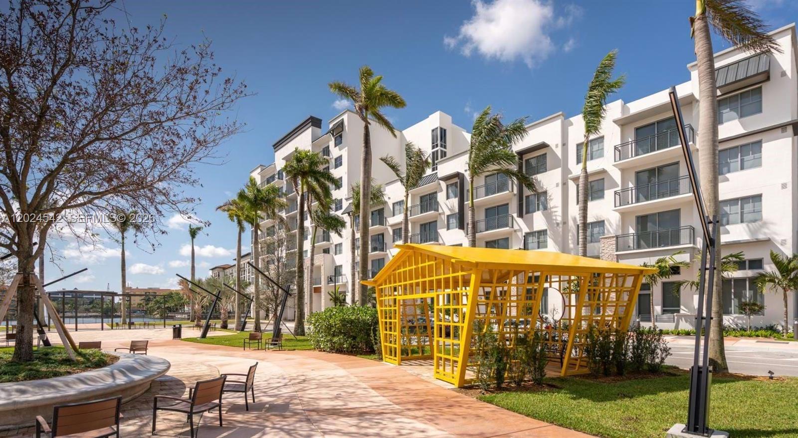 A yellow lattice gazebo sits on a paved walkway near a modern apartment building — 4720 NW 85th Ave, Doral FL 33166, DORAL, FL