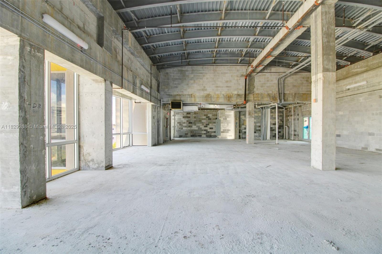 An unfinished commercial space features exposed concrete walls, a metal ceiling, and large glass windows — 6930 Collins Ave, Miami Beach FL 33141, MIAMI BEACH, FL