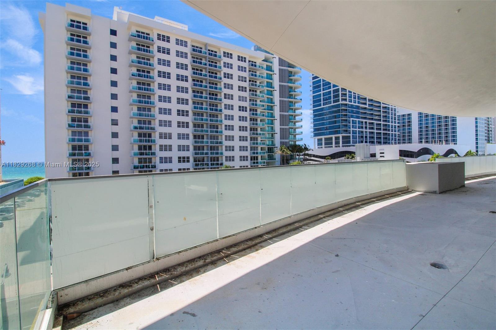 A spacious balcony with a glass railing overlooks high-rise buildings and the ocean — 6930 Collins Ave, Miami Beach FL 33141, MIAMI BEACH, FL