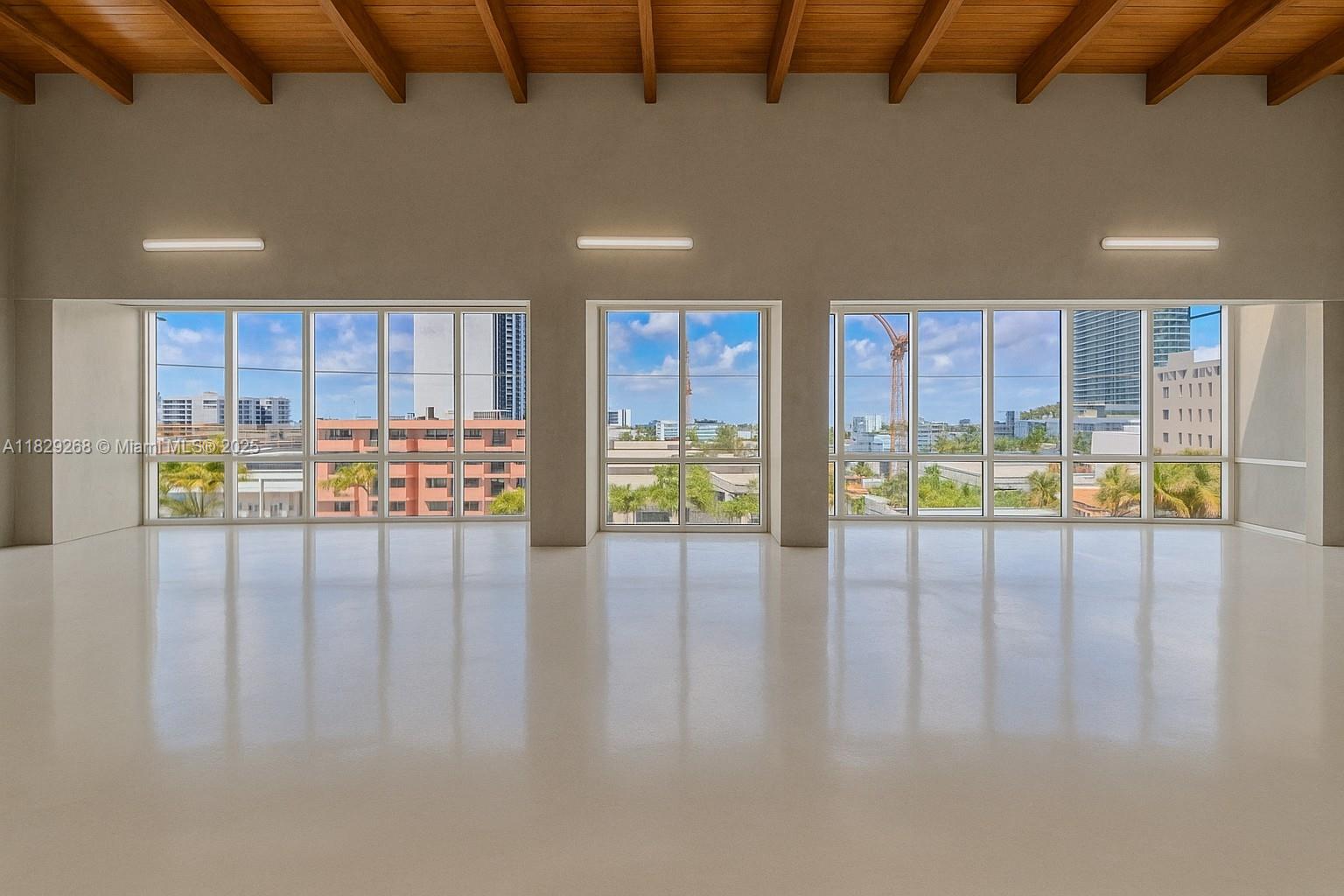 An empty room features white floors, a wood-beamed ceiling, and large windows overlooking a city — 6930 Collins Ave, Miami Beach FL 33141, MIAMI BEACH, FL