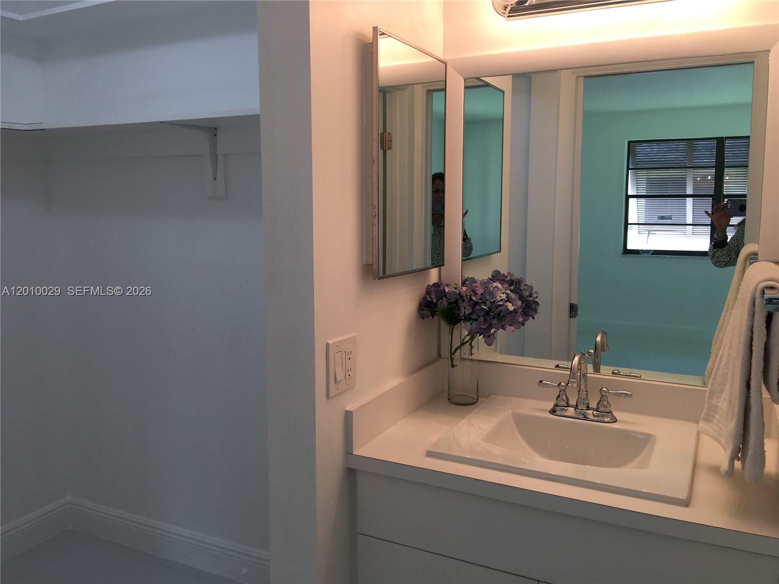 A bathroom vanity with a white countertop, sink, mirror, and an adjacent closet area — 7995 SW 86th St # 322, Miami FL 33143, MIAMI, FL