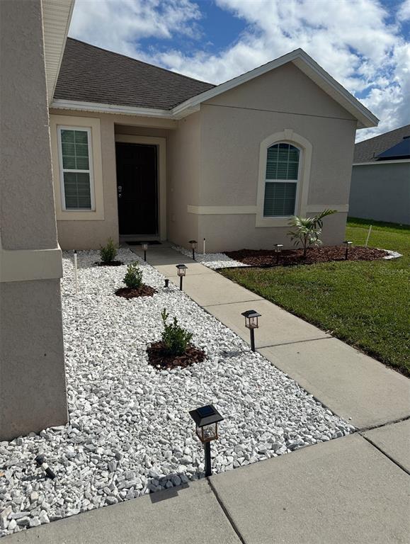 A beige house exterior features a concrete walkway, white rock landscaping, and solar path lights — 724 LAKE CUMMINGS BOULEVARD, LAKE ALFRED, FL