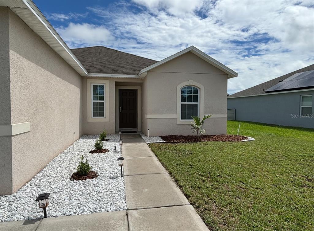 The exterior of a beige stucco house features a concrete walkway, white gravel, and landscaping — 724 LAKE CUMMINGS BOULEVARD, LAKE ALFRED, FL