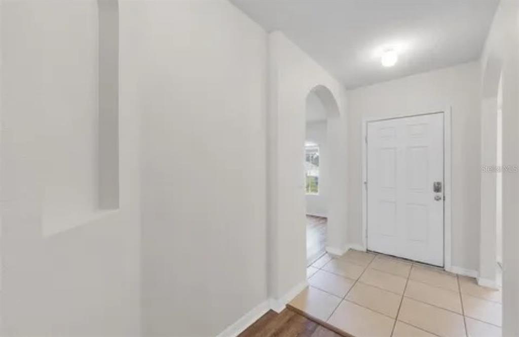 An entryway with tiled flooring, a white front door, and an arched doorway to another room — 724 LAKE CUMMINGS BOULEVARD, LAKE ALFRED, FL