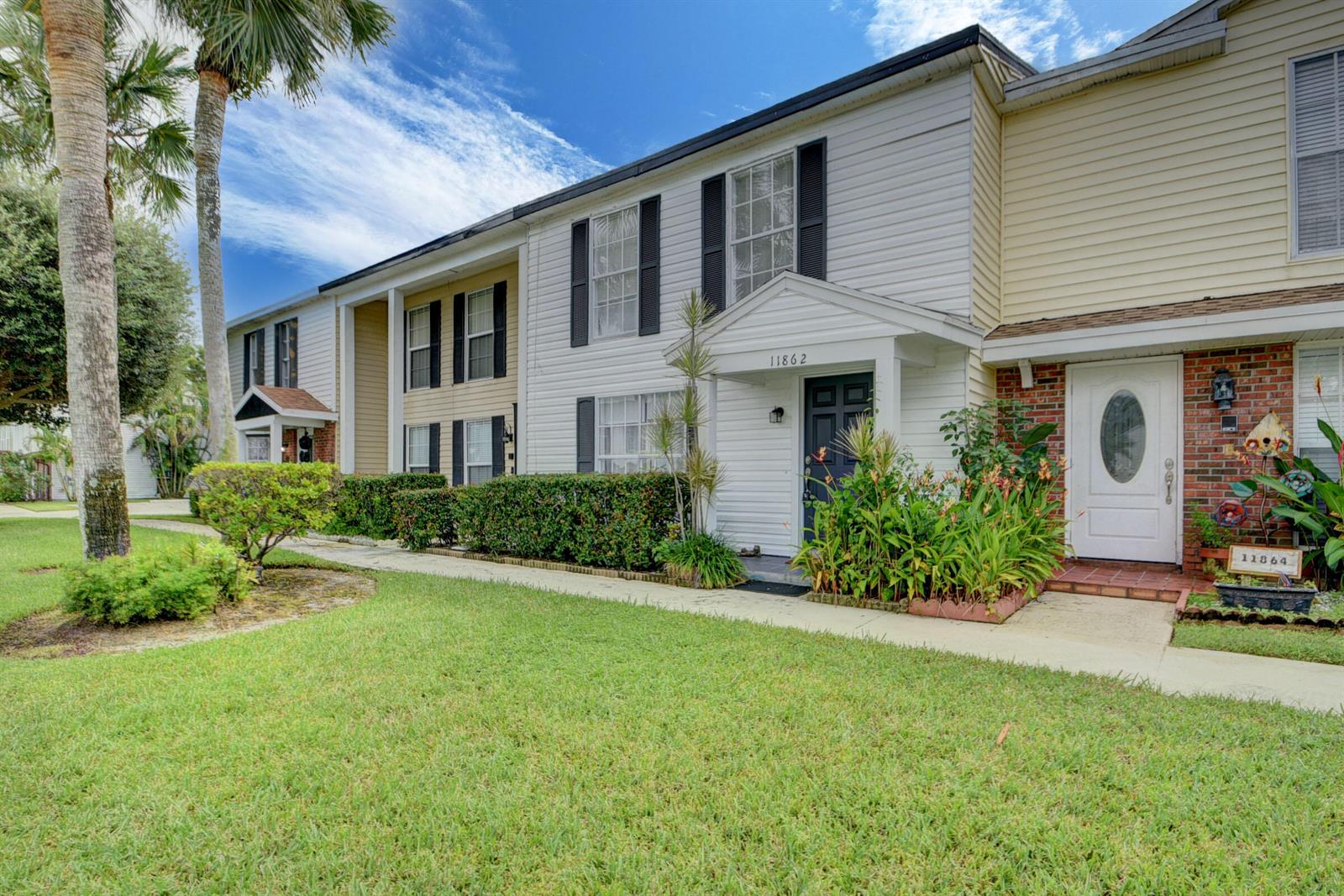 A two-story townhouse exterior features white siding, black shutters, and a small front garden — 11862 E Brier Patch Ct Court, Wellington FL 33414, WELLINGTON, FL