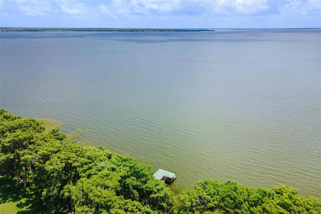 An aerial view shows a small dock extending into a large lake from a wooded shoreline — 29205 S CORLEY ISLAND ROAD, LEESBURG, FL