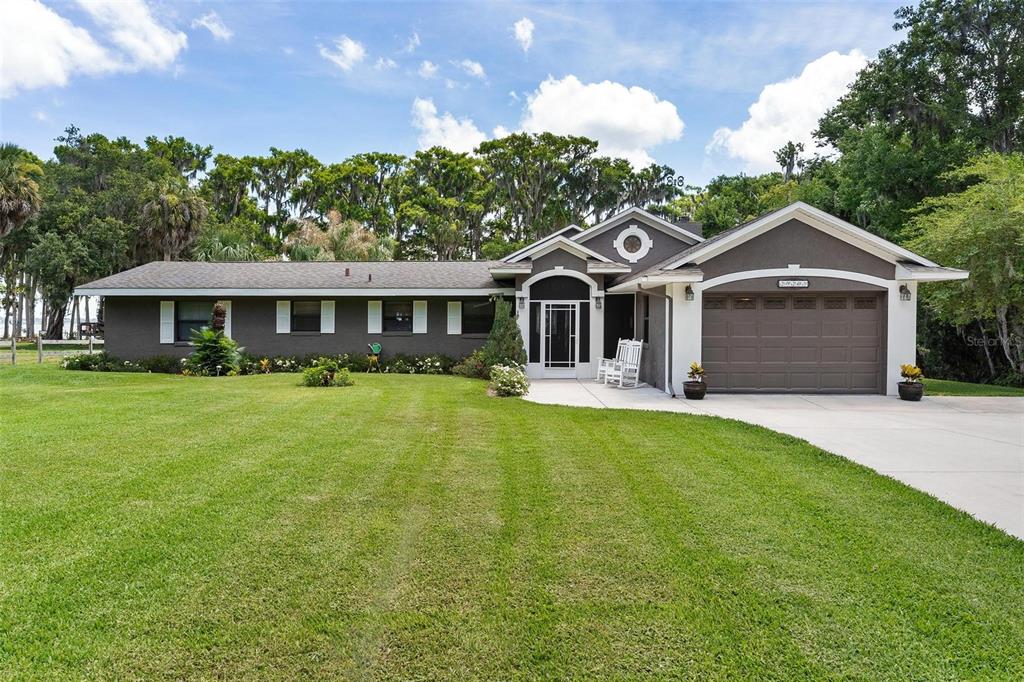 A single-story house with a dark gray exterior, a two-car garage, and a large lawn — 29205 S CORLEY ISLAND ROAD, LEESBURG, FL