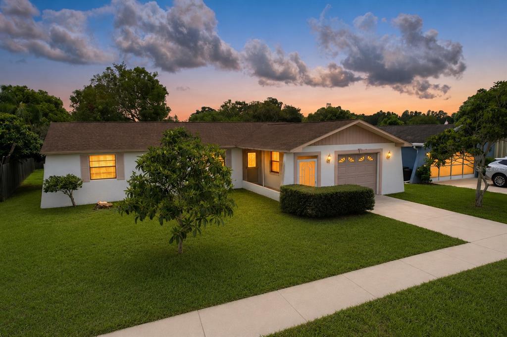A single-story house with a white exterior, brown roof, and a green lawn at sunset — 12132 SHADOW RIDGE BOULEVARD, HUDSON, FL