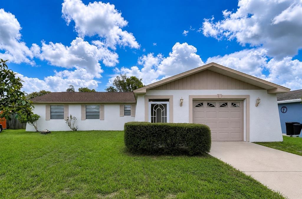 A single-story house with a white stucco exterior, a tan garage door, and a front lawn — 12132 SHADOW RIDGE BOULEVARD, HUDSON, FL