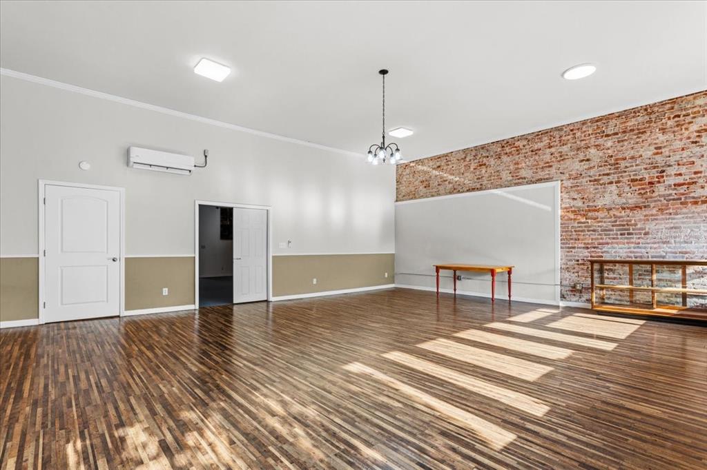 A spacious room features hardwood floors, a brick accent wall, and a white wainscoted wall — 14827 MAIN STREET, ALACHUA, FL
