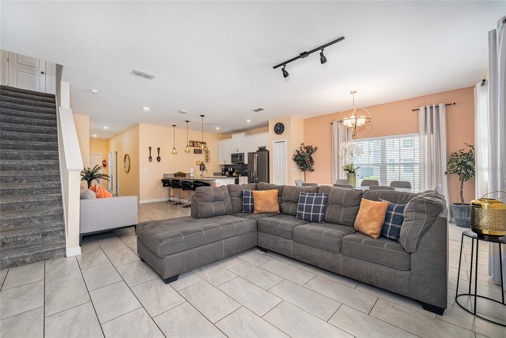A living room with a gray sectional sofa, tiled floors, and an open-concept kitchen — 4800 MEMORIES LANE, KISSIMMEE, FL