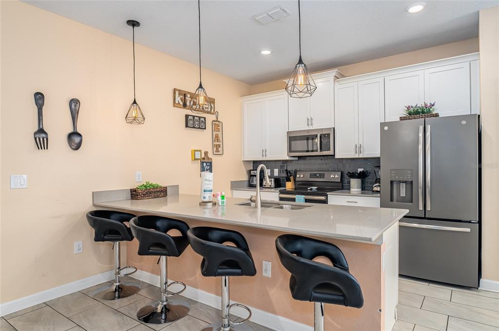 A kitchen features white cabinets, stainless steel appliances, a quartz island, and four black barstools — 4800 MEMORIES LANE, KISSIMMEE, FL