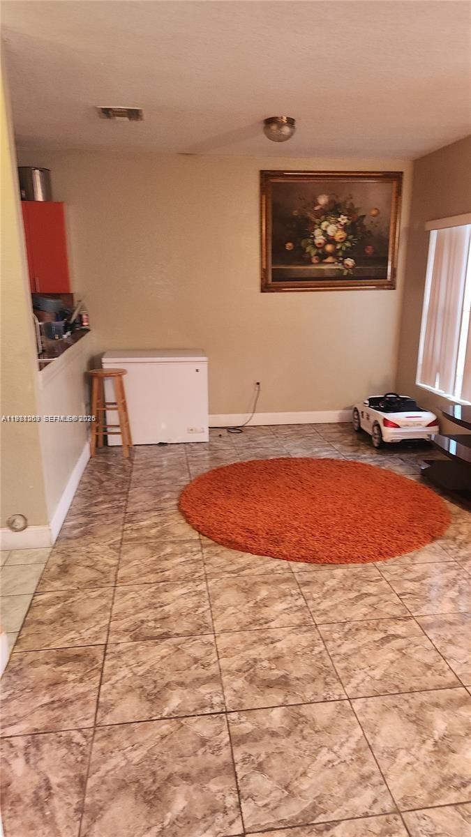 A room with tiled floors, a round orange rug, a chest freezer, and wall art — 18963 SW 113th Ct, Miami FL 33157, MIAMI, FL