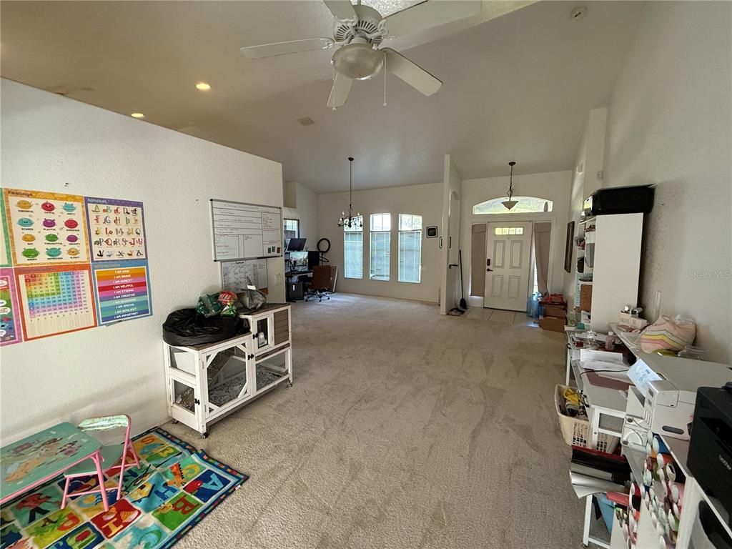A spacious living area features beige carpeting, high ceilings, a ceiling fan, and educational wall posters — 4619 ITALY AVENUE, NORTH PORT, FL