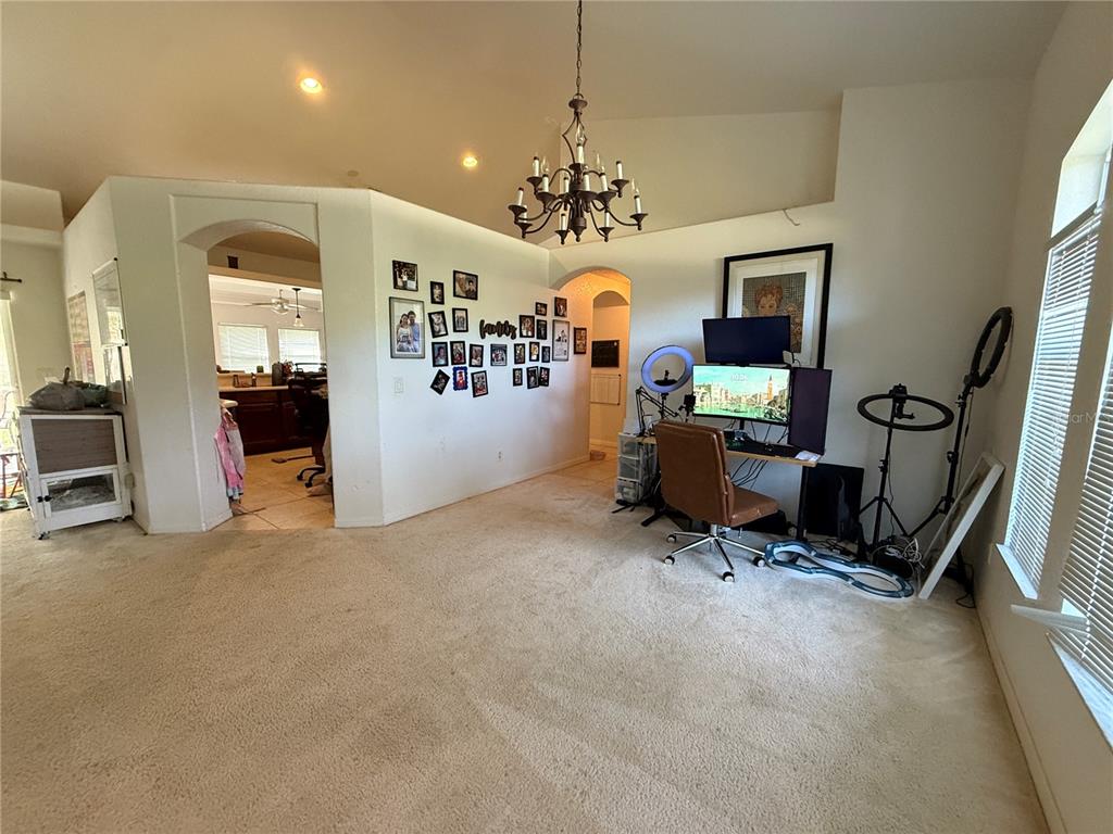 A carpeted living area features a desk setup, a gallery wall, and an arched entryway — 4619 ITALY AVENUE, NORTH PORT, FL