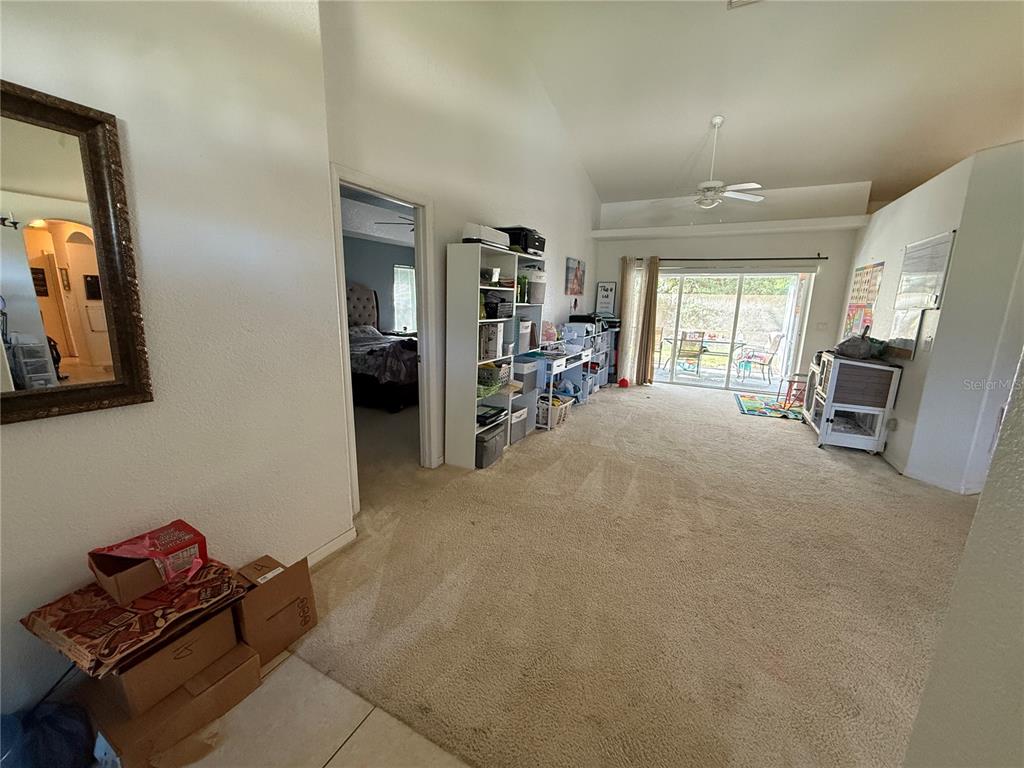 A carpeted living room features a tall shelving unit, a doorway to a bedroom, and sliding doors — 4619 ITALY AVENUE, NORTH PORT, FL