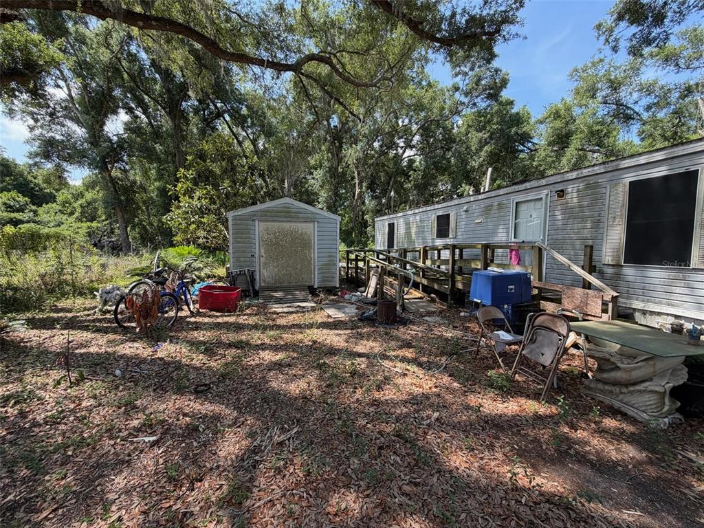An outdoor view shows a mobile home with a wooden ramp, a shed, and scattered items — 369 CR 552N, BUSHNELL, FL