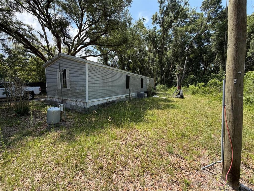 An exterior view of a single-wide mobile home situated on a grassy, wooded lot — 369 CR 552N, BUSHNELL, FL