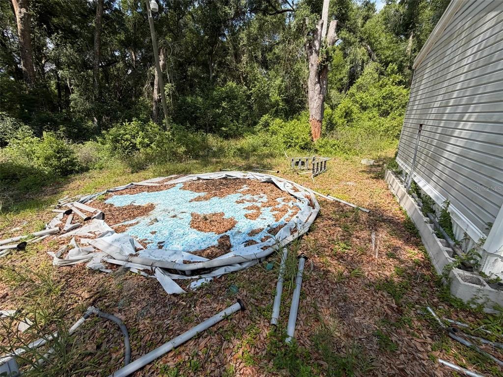 A collapsed above-ground pool sits in a backyard next to the side of a house — 369 CR 552N, BUSHNELL, FL