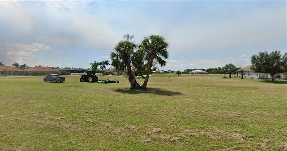 A tractor mows a large, flat, grassy lot featuring a central palm tree — 24465 SAN RAFAEL ROAD, PUNTA GORDA, FL