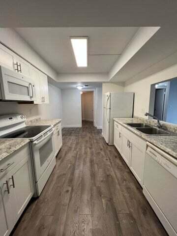 A galley-style kitchen features white cabinets, stainless steel appliances, and wood-look flooring — 825 Egret Circle # 404, Delray Beach FL 33444, DELRAY BEACH, FL