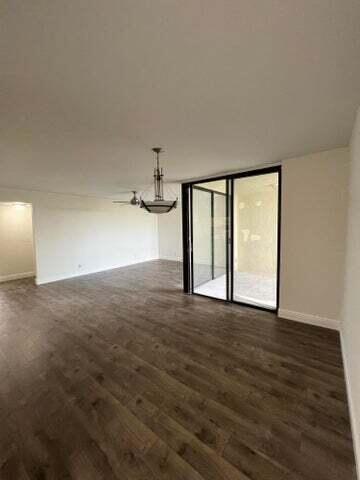 An empty living room features wood-look flooring, a ceiling fan, and sliding glass balcony doors — 825 Egret Circle # 404, Delray Beach FL 33444, DELRAY BEACH, FL