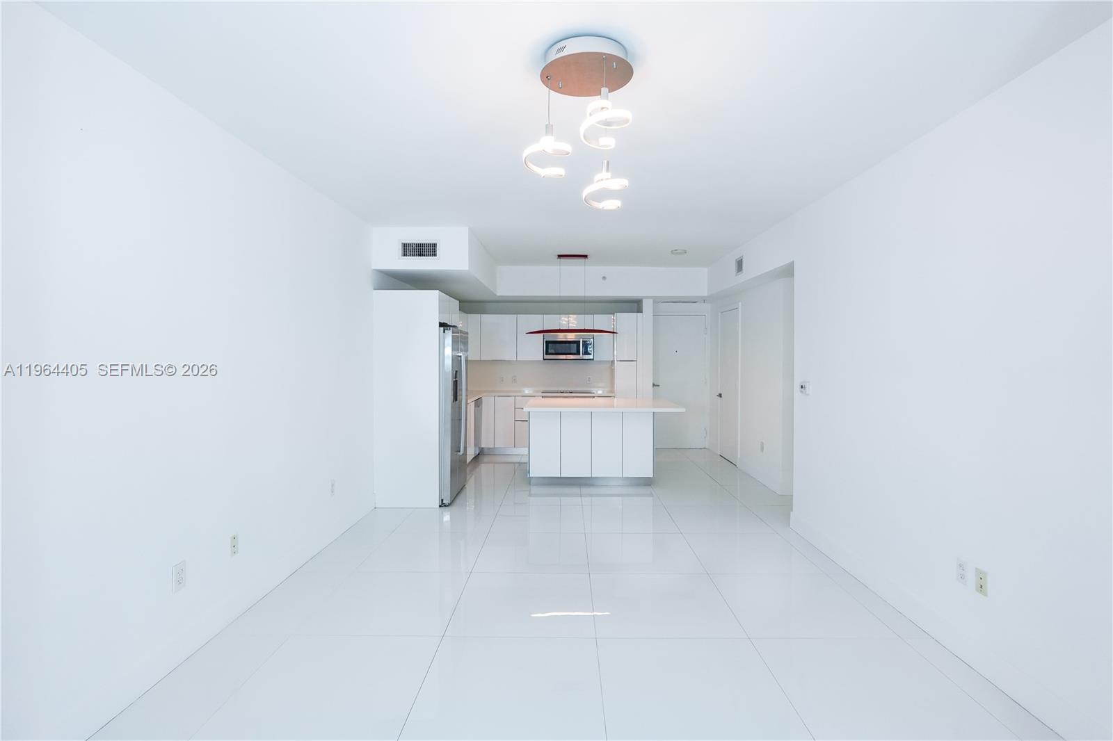 A minimalist kitchen with white cabinetry and tile flooring opens into a spacious living area — 1010 SW 2nd Ave # 606, Miami FL 33130, MIAMI, FL