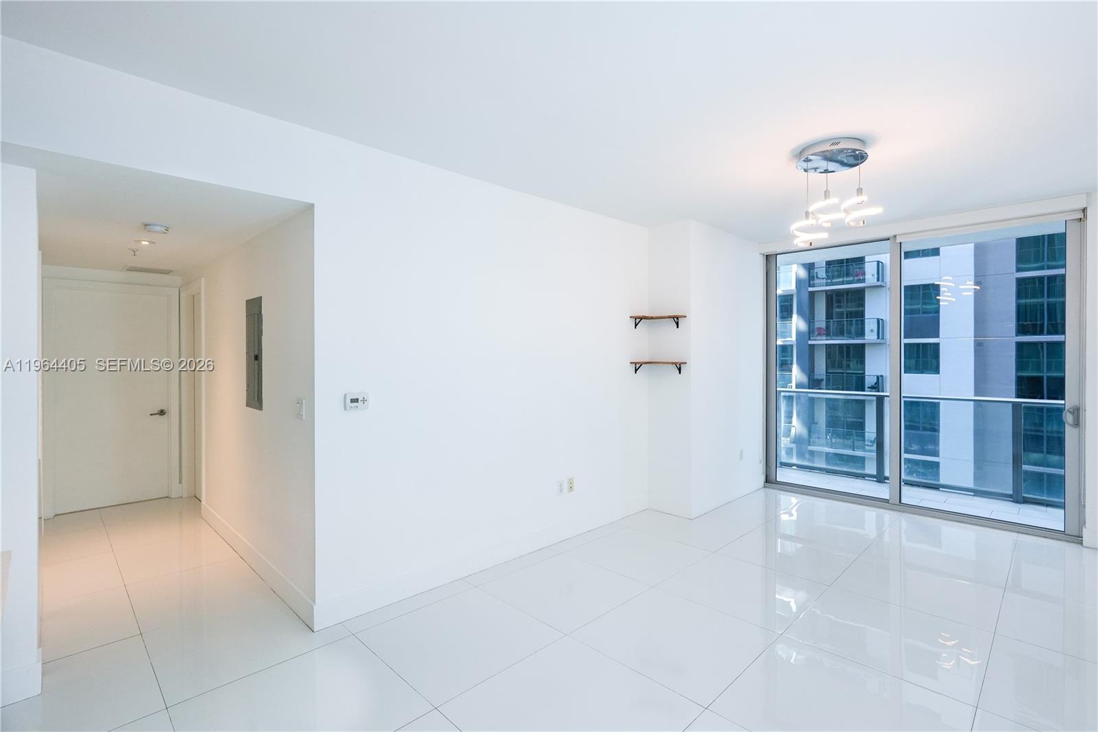 A bright, minimalist living space features white tile floors, a modern light fixture, and balcony access — 1010 SW 2nd Ave # 606, Miami FL 33130, MIAMI, FL