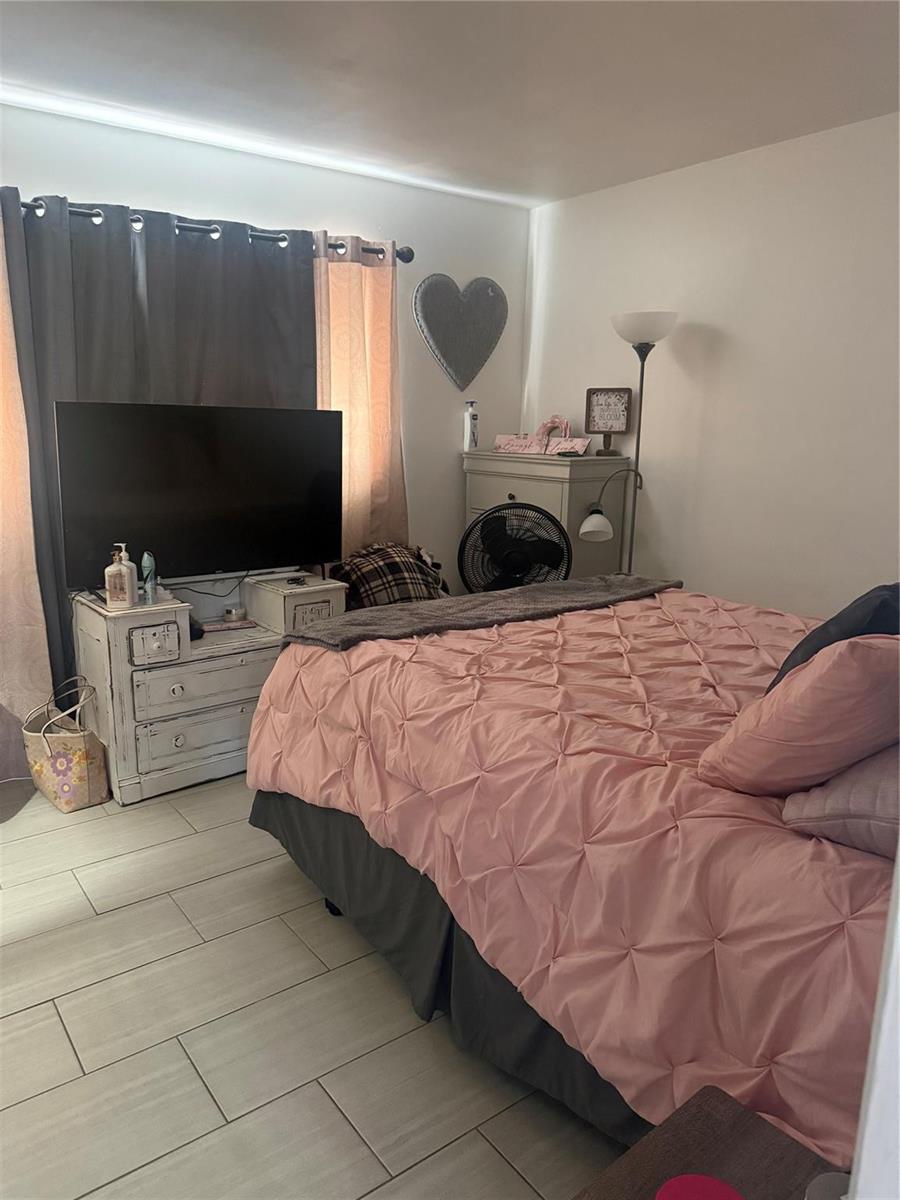 A bedroom features a pink tufted comforter, a television on a dresser, and tile flooring — 817 SE 9th Street, Okeechobee FL 34974, OKEECHOBEE, FL